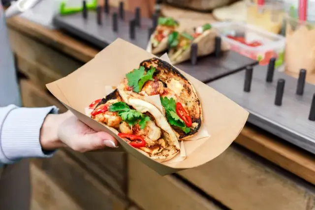Tacos en barquette kraft tenus à la main devant le food truck
